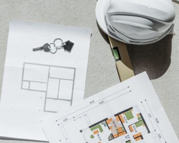 white hard hat beside floor plans and house key