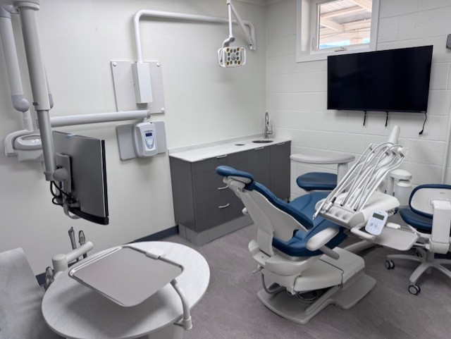 Modern dental operatory with blue chair, overhead light, and wall-mounted TV.